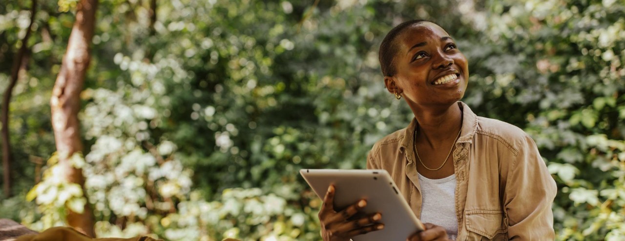 smiling person looking skywards in forest with tablet device
